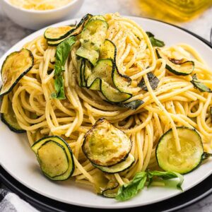 Plate of pasta alla Nerano with saut&eacute;ed zucchini slices and fresh basil, served with a fork and a checked napkin nearby.