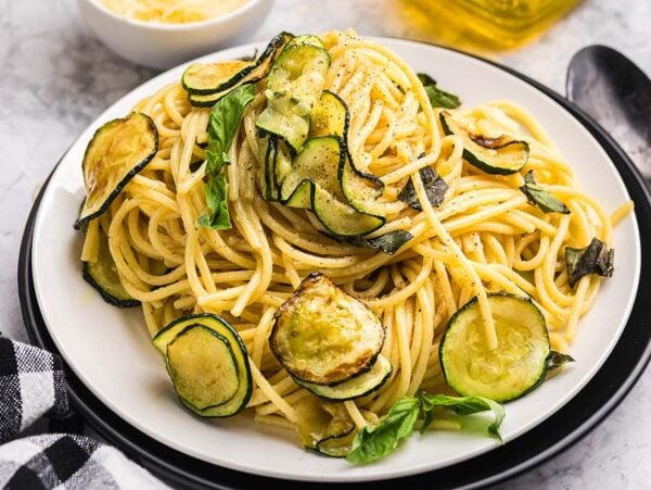 Plate of pasta alla Nerano with sautéed zucchini slices and fresh basil, served with a fork and a checked napkin nearby.