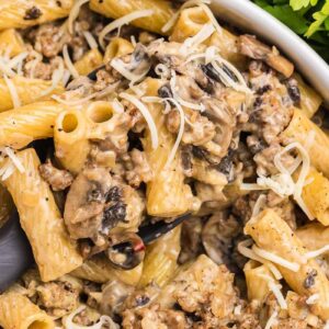 Creamy rigatoni pasta alla Norcina with ground beef, mushrooms, and shredded cheese in a white bowl, garnished with parsley.