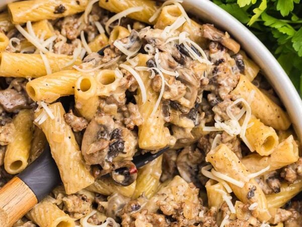 Creamy rigatoni pasta alla Norcina with ground beef, mushrooms, and shredded cheese in a white bowl, garnished with parsley.