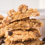 A stack of Peanut Butter Snickers Cookies drizzled with peanut butter, with a white ramekin in the background.