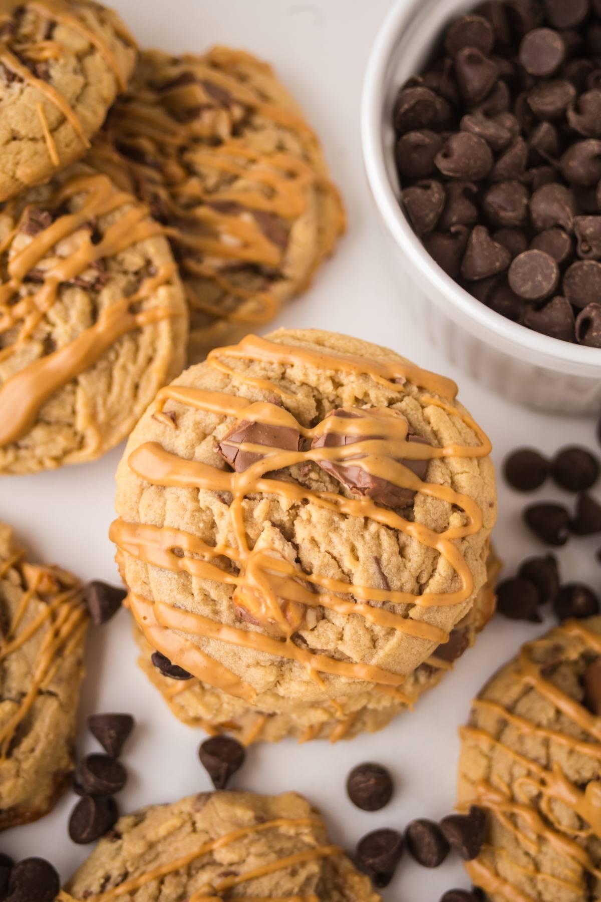 Peanut butter cookies drizzled with caramel, surrounded by chocolate chips and a bowl of chocolate chips.
