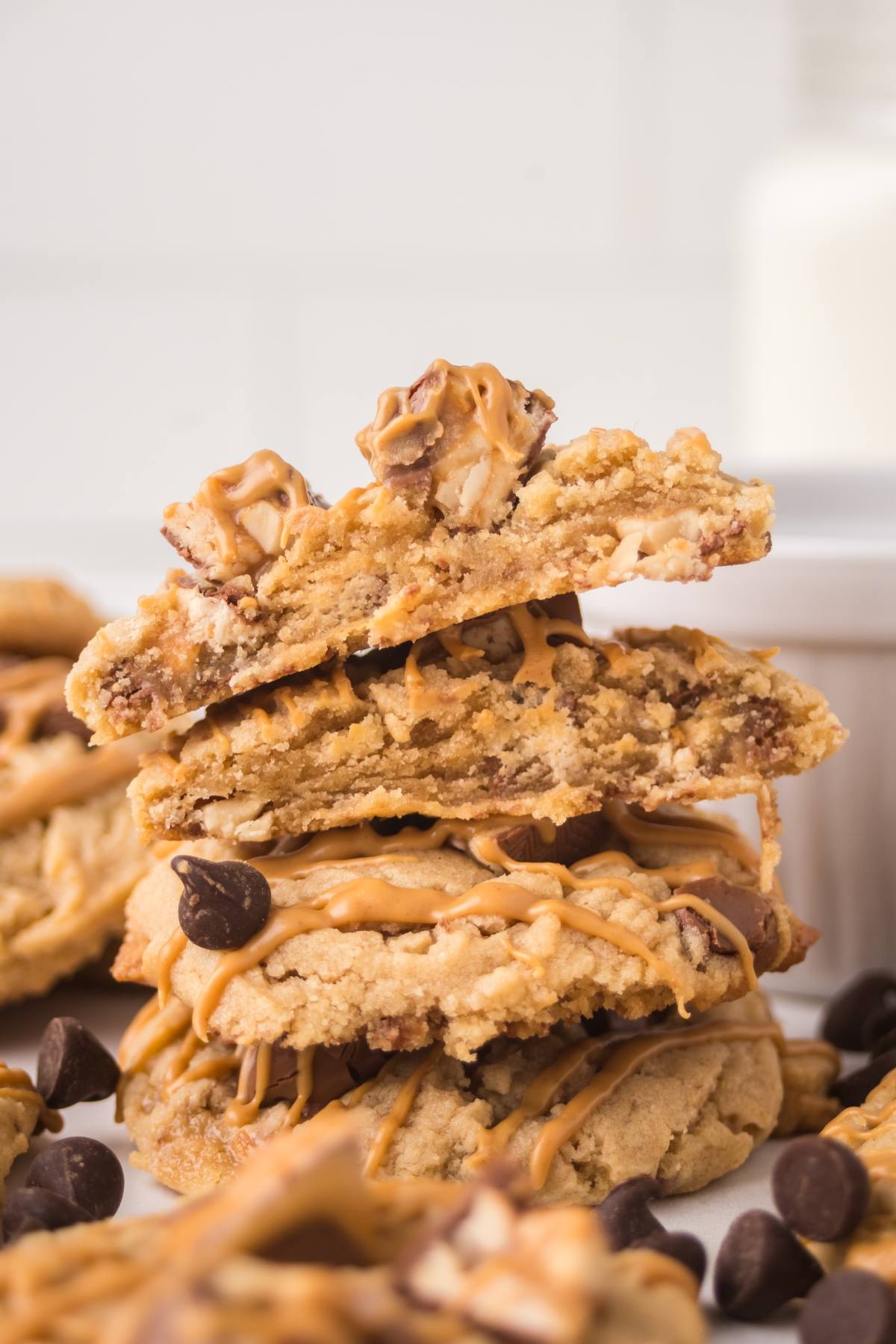 Stacked cookies with chocolate chips and peanut butter drizzle, broken to show the soft, chunky inside.