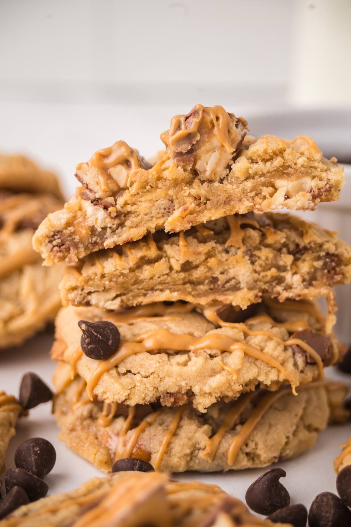Stack of peanut butter cookies with chocolate chips, drizzled with peanut butter, and broken in half on top.
