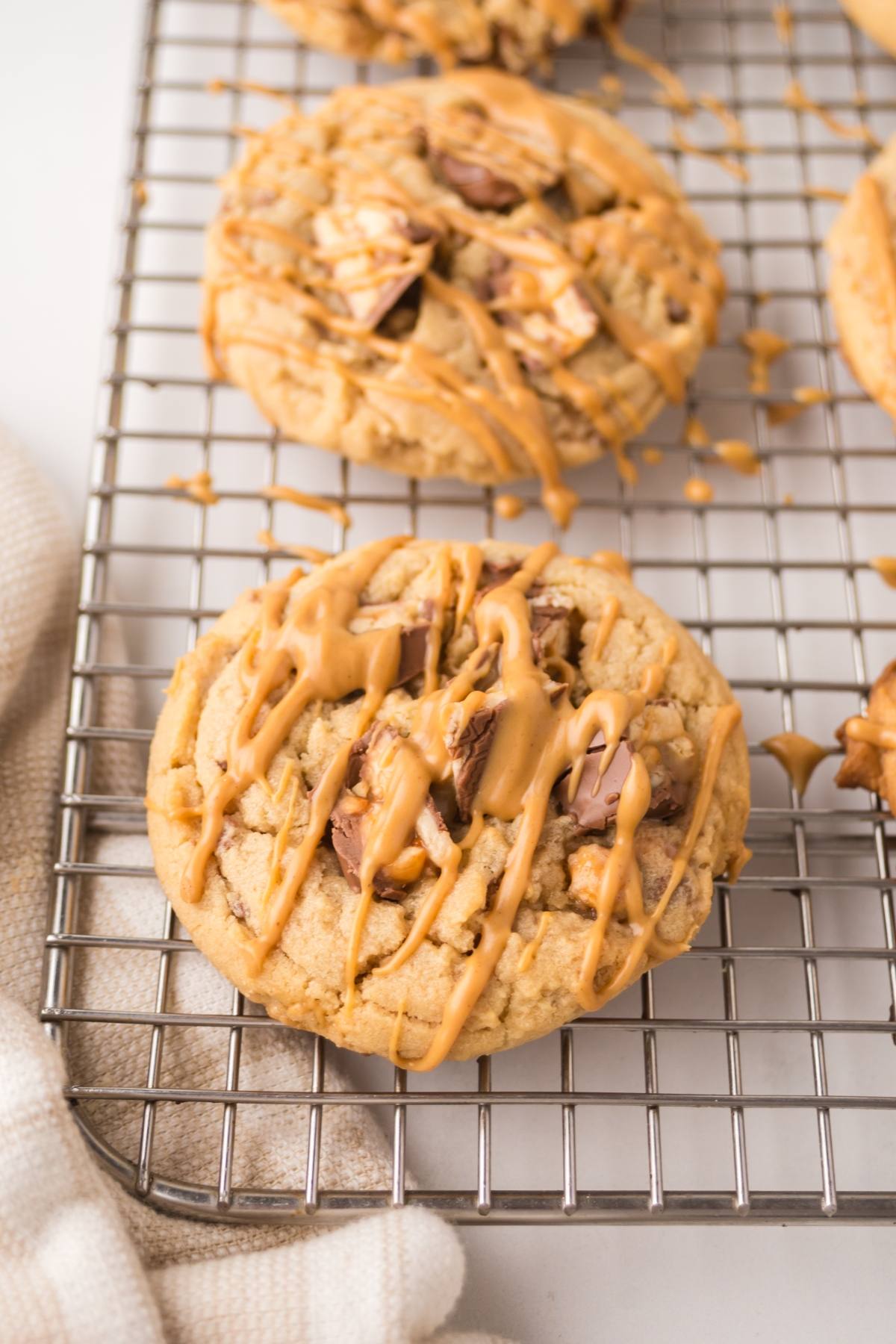 Close-up of a cookie with chocolate chunks and caramel drizzle on a cooling rack.