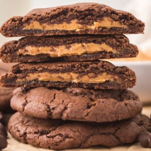 Three Peanut Butter Stuffed Chocolate Cookies, stacked on more cookies, showcase their rich peanut butter filling, with chocolate chips scattered around them.