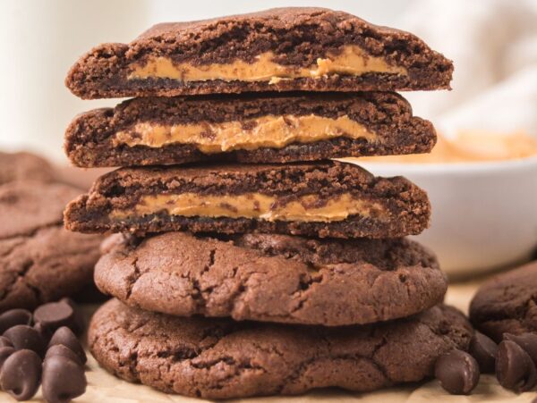 Three Peanut Butter Stuffed Chocolate Cookies, stacked on more cookies, showcase their rich peanut butter filling, with chocolate chips scattered around them.