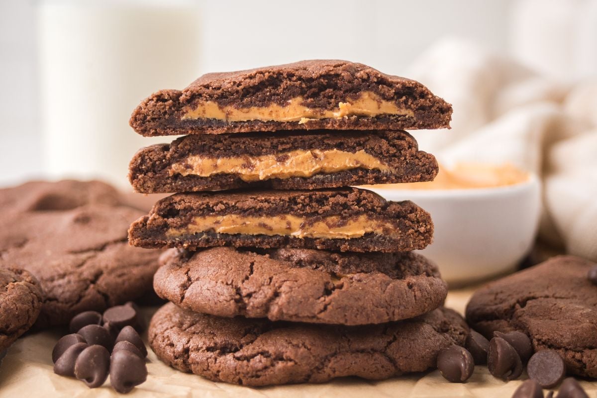 A stack of Peanut Butter Stuffed Chocolate Cookies with creamy filling, surrounded by chocolate chips and a bowl in the background.