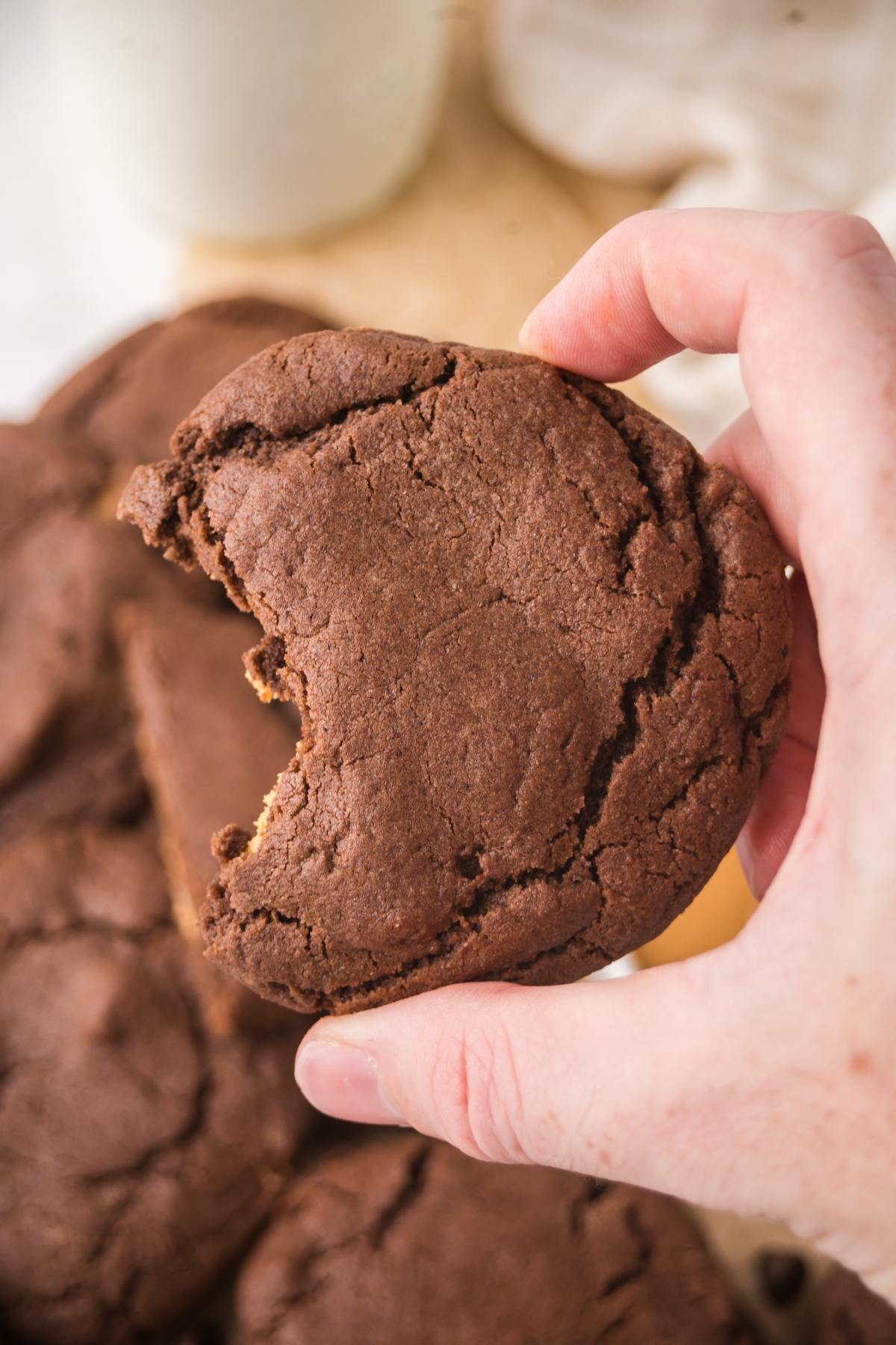 A hand holding a chocolate cookie with a bite taken out of it.