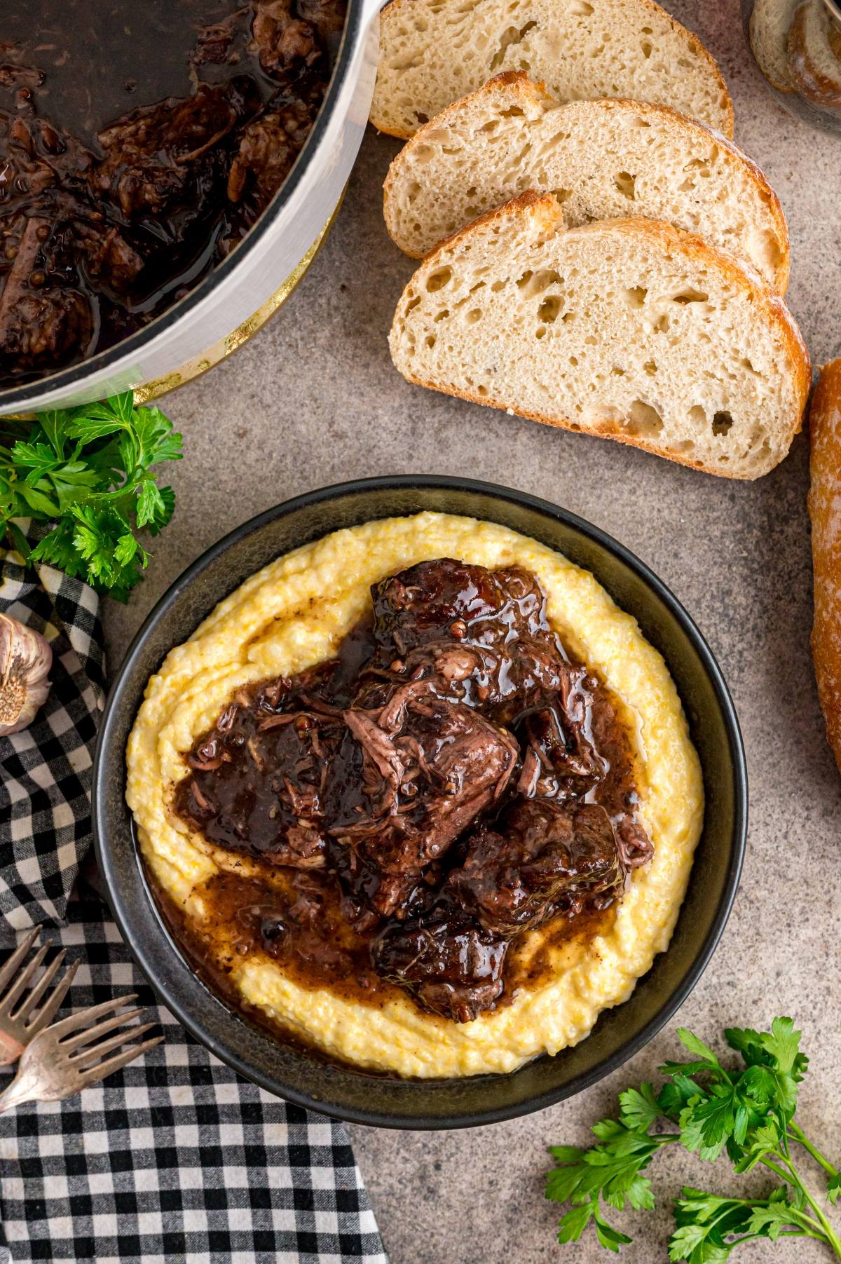 A bowl of creamy polenta topped with braised beef, served with slices of rustic bread on the side.