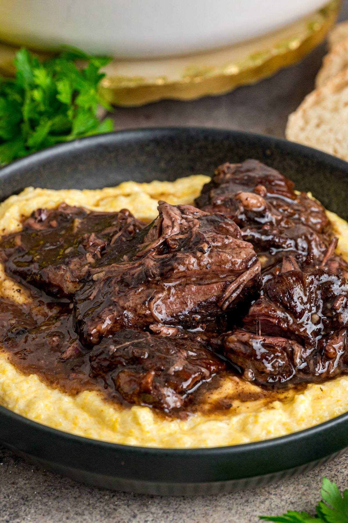 Braised beef in a rich, dark sauce served over creamy polenta in a black bowl.