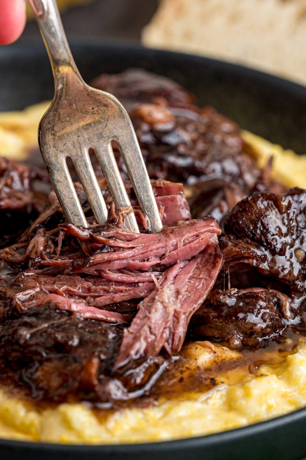 A fork shredding tender braised beef over creamy mashed potatoes.