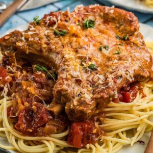 Pork chops Italiano with savory tomato sauce served over spaghetti on a white plate, garnished with fresh herbs and grated cheese.