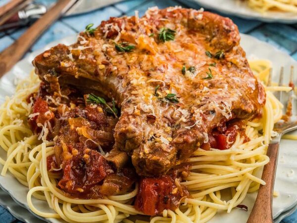 Pork chops Italiano with savory tomato sauce served over spaghetti on a white plate, garnished with fresh herbs and grated cheese.