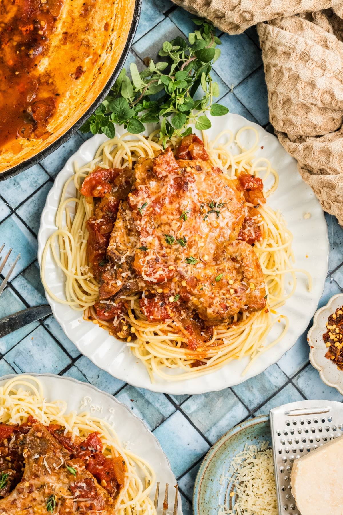 Plate of spaghetti topped with tomato sauce and meat, garnished with herbs, on a tiled blue surface.