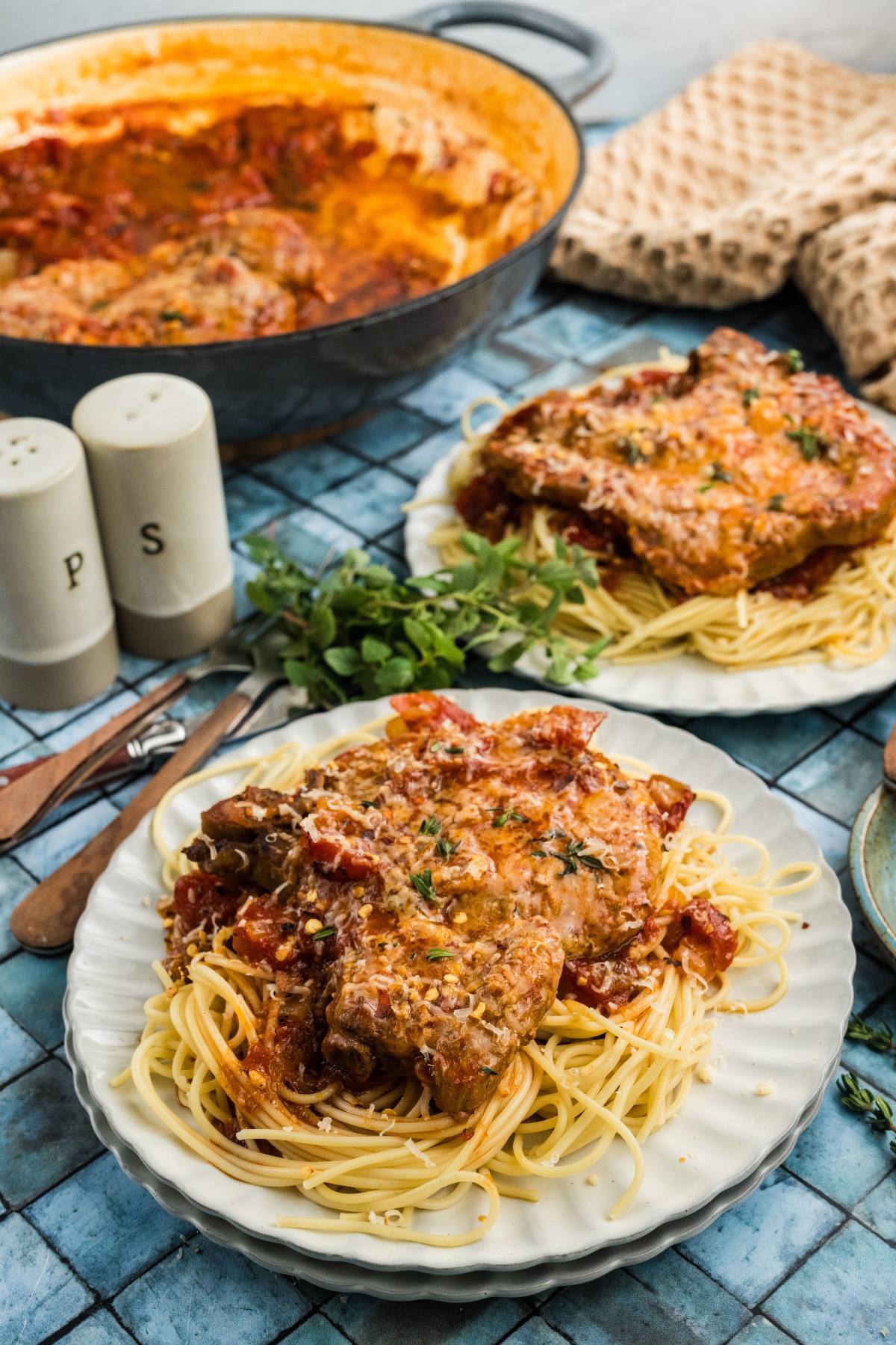 Plates of spaghetti topped with breaded meat and tomato sauce, with a pot of sauce in the background.