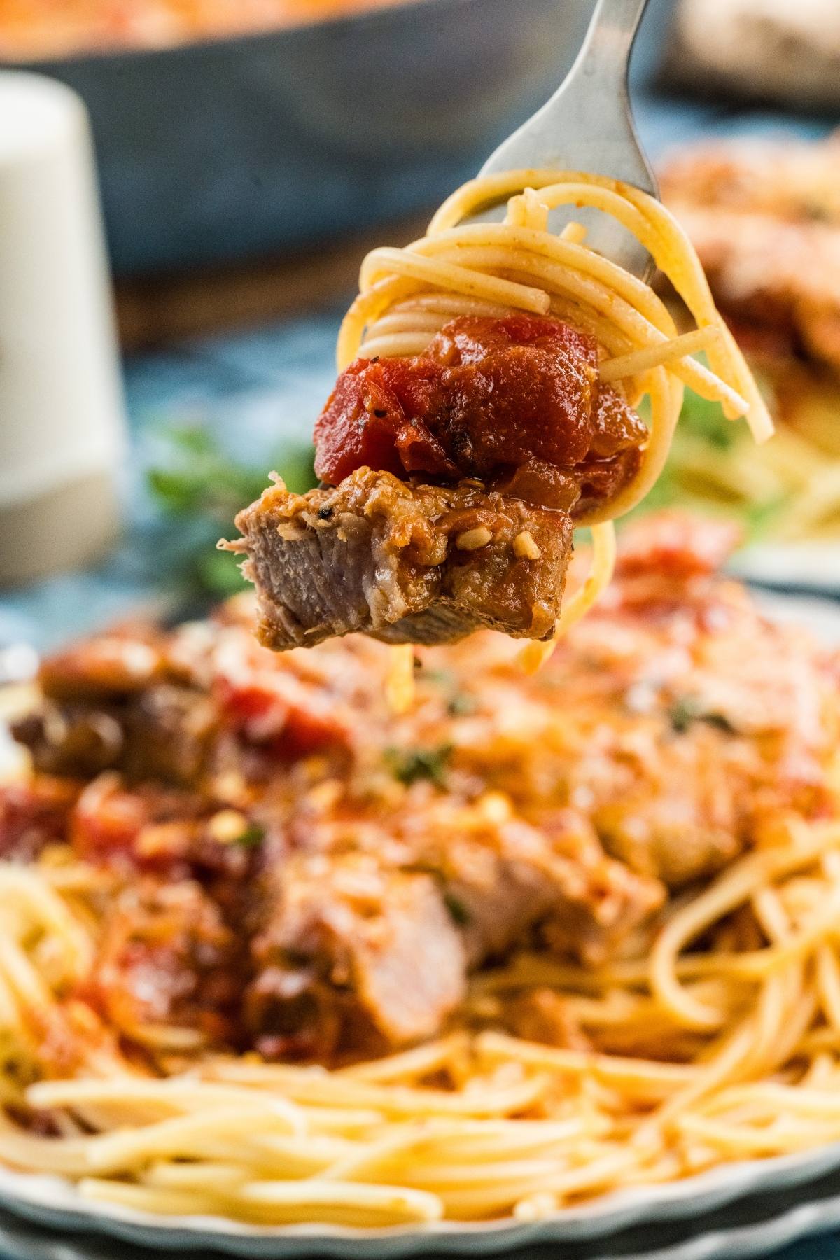 A fork holds spaghetti and a chunk of meat topped with tomato sauce above a plate of pasta.