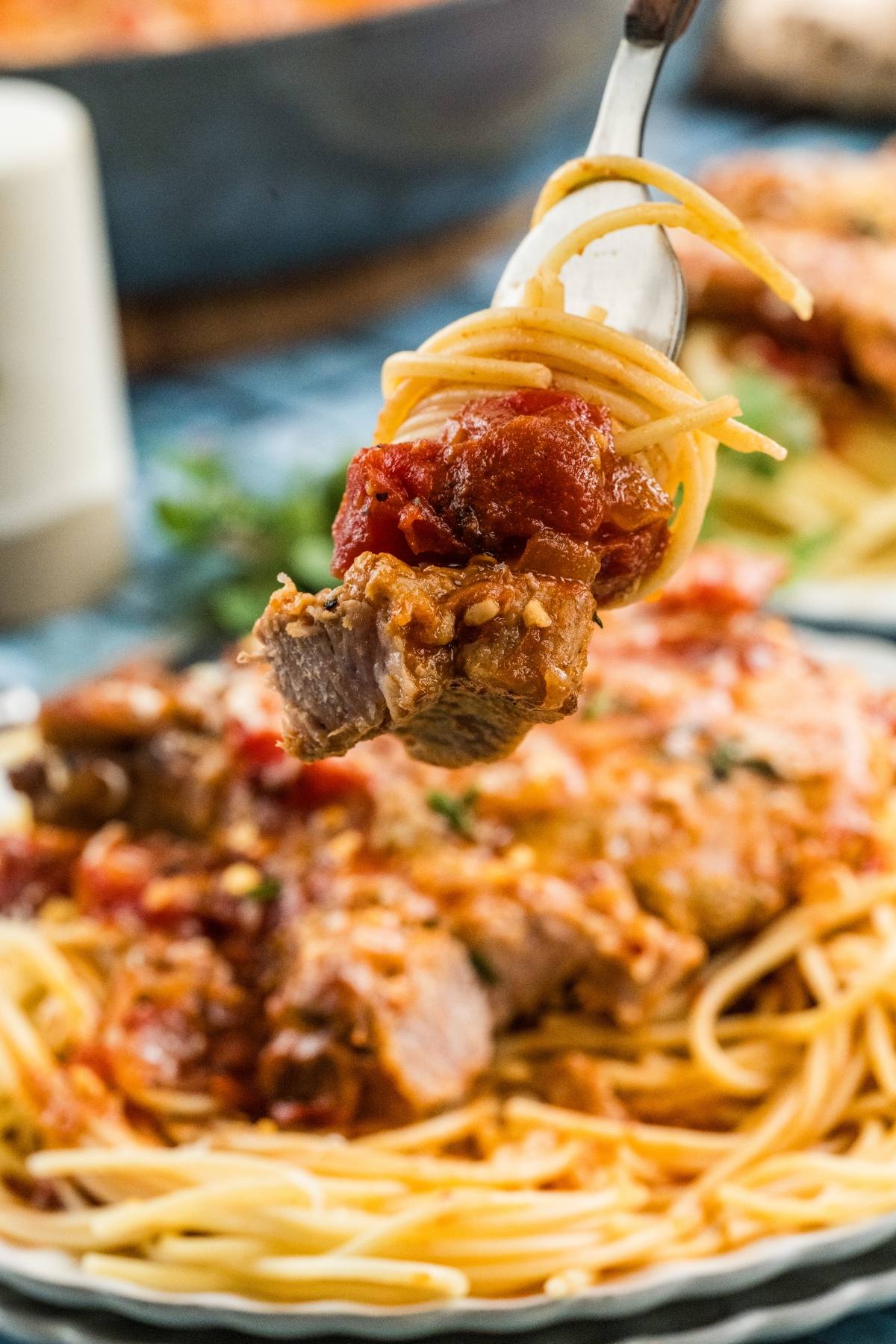 A fork holds spaghetti, tomato sauce, and a piece of meat above a plate of pasta.