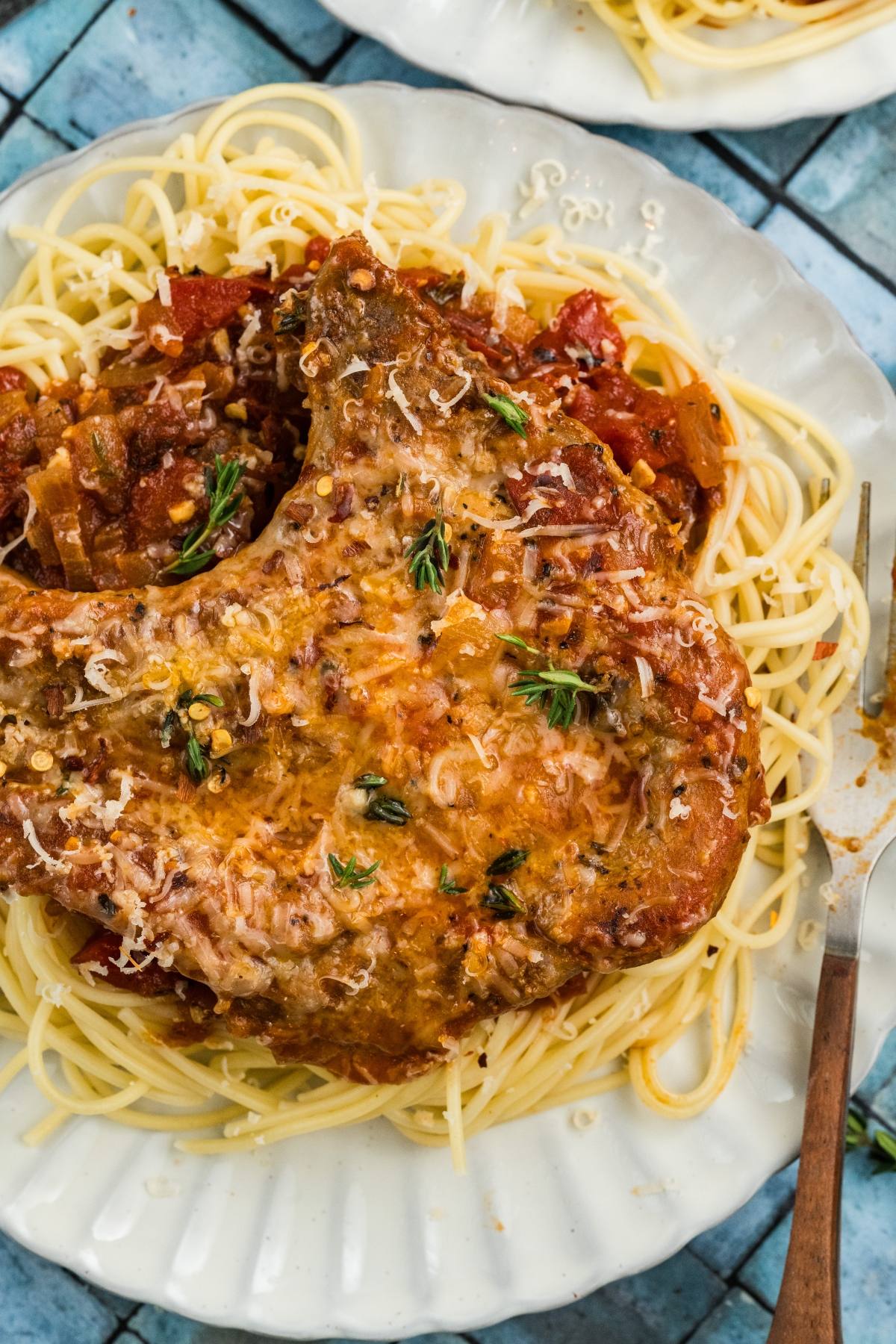 Pork chop with herbs and tomato sauce served on spaghetti noodles on a white plate.