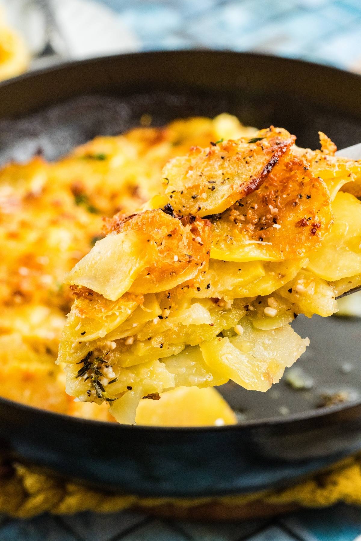 A close-up of a spoon lifting cheesy, baked potatoes galette from a skillet.