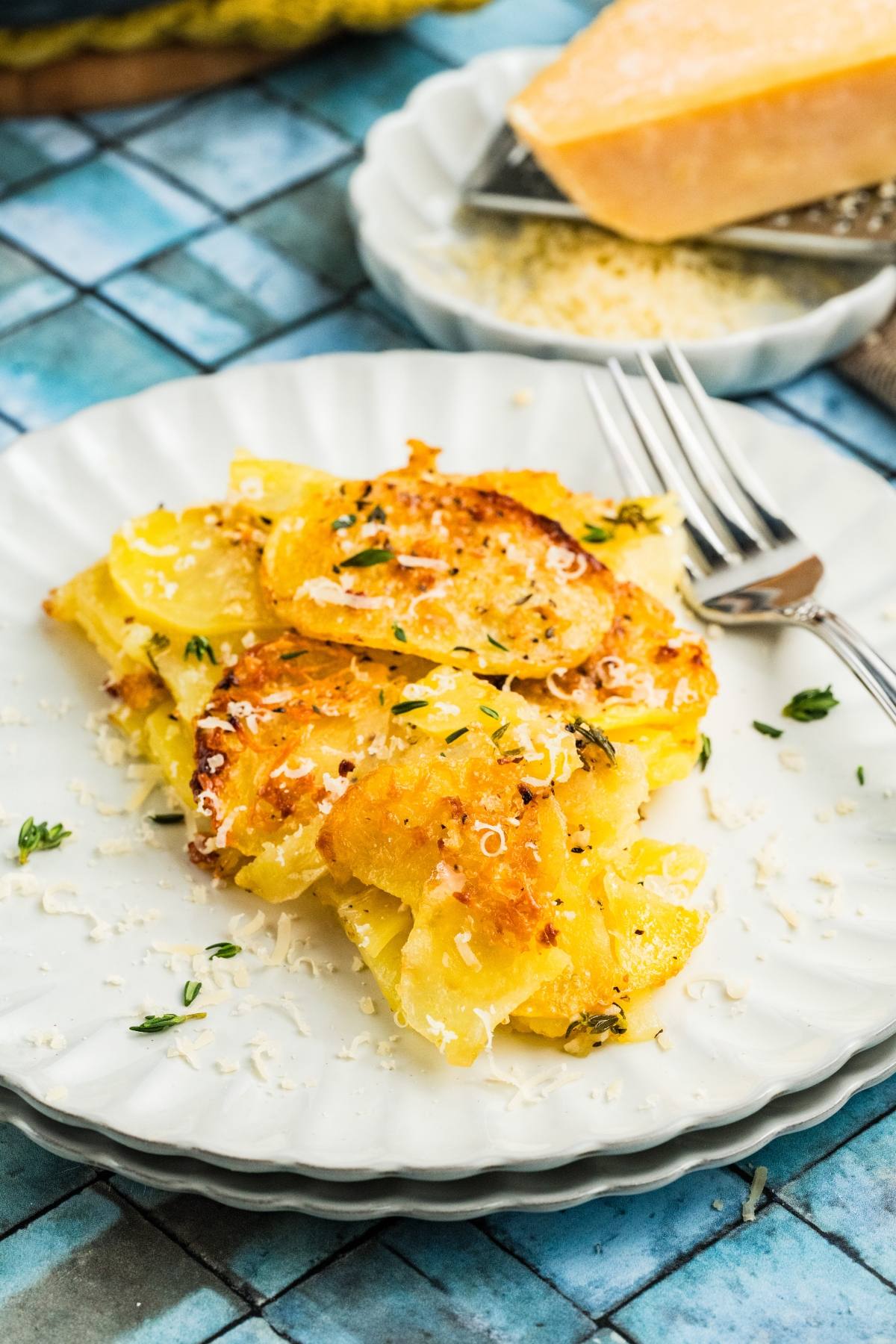 A serving of cheesy scalloped potatoes galette garnished with herbs on a white plate with a fork.