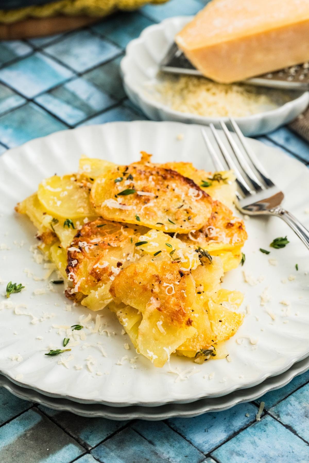 A serving of cheesy potato galette topped with herbs and grated cheese on a white plate with a fork.