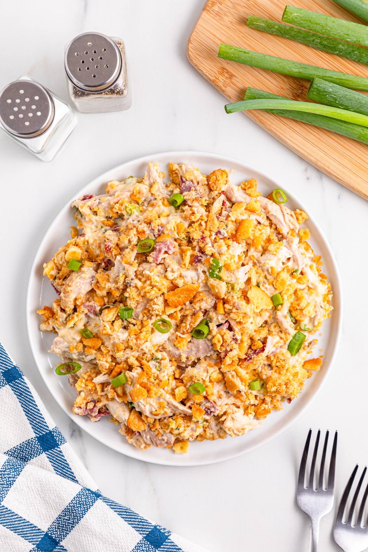 A plate of chicken casserole topped with green onions, next to salt, pepper, green onions, and utensils.