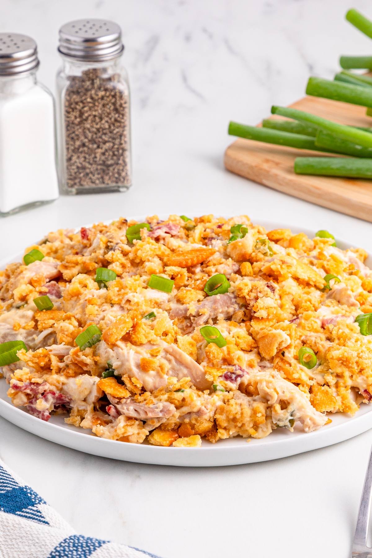 A plate of creamy chicken casserole topped with crumbled crackers and sliced green onions sits on a table.