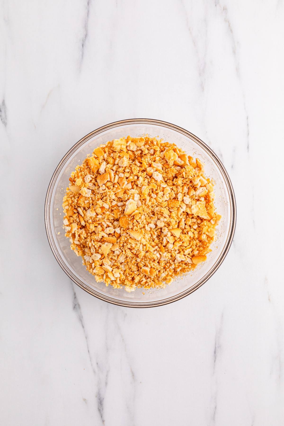 A glass bowl filled with crushed crackers on a white marble surface.