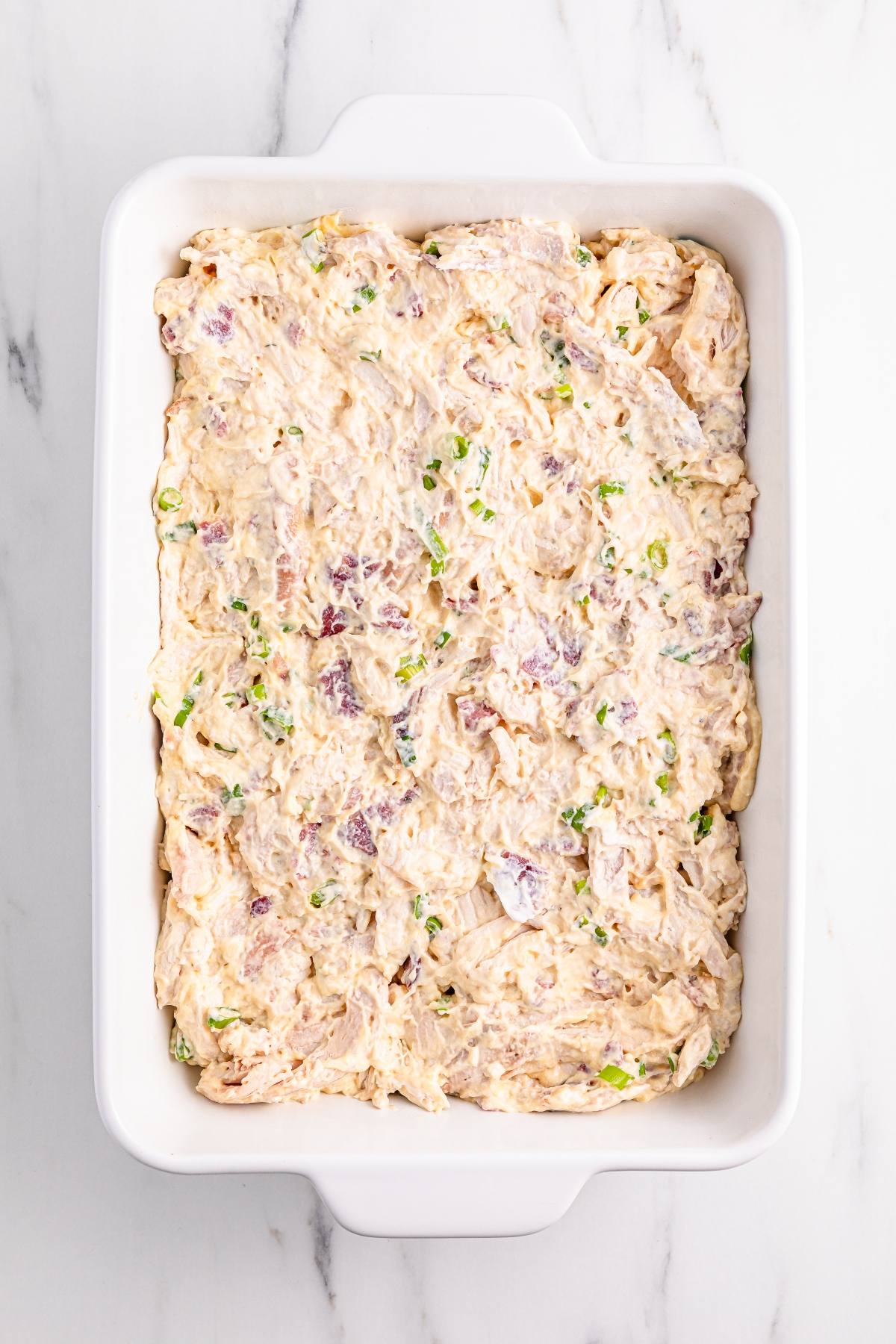 A white baking dish filled with a creamy, mixed casserole topped with chopped green onions.