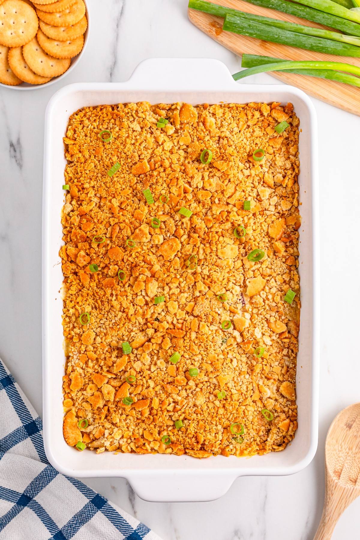 Casserole topped with crushed crackers and green onions in a white dish, with crackers and green onions nearby.