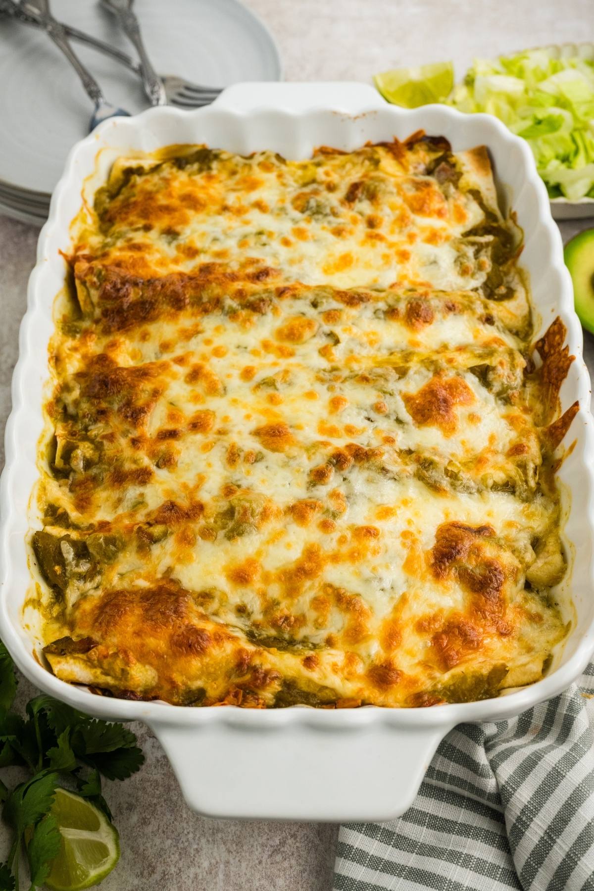 A baked casserole dish with golden, melted cheese on top, surrounded by plates and fresh vegetables.