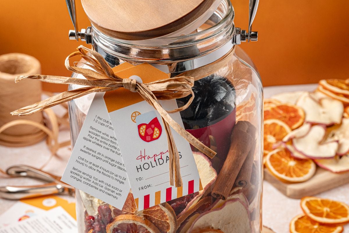 A Sangria Kit Gift Jar filled with dried citrus slices and cinnamon sticks, labeled “Happy Holidays” with a festive gift tag.