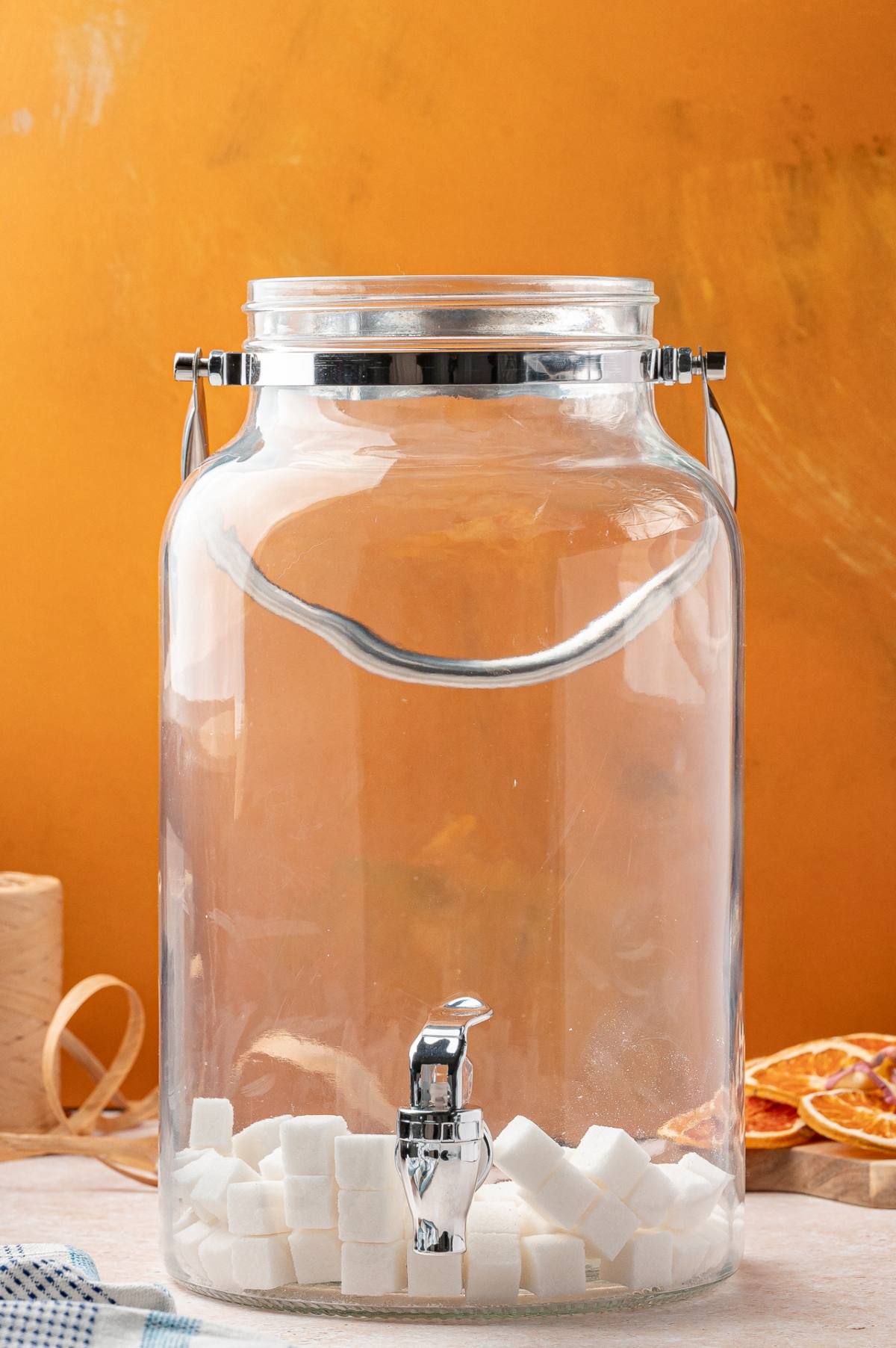 A large glass beverage dispenser with a metal spigot, containing several sugar cubes at the bottom.