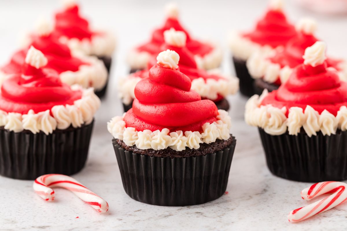 Santa Hat Cupcakes with chocolate bases and red and white frosting, topped to resemble Santa’s hat and surrounded by festive small candy canes.