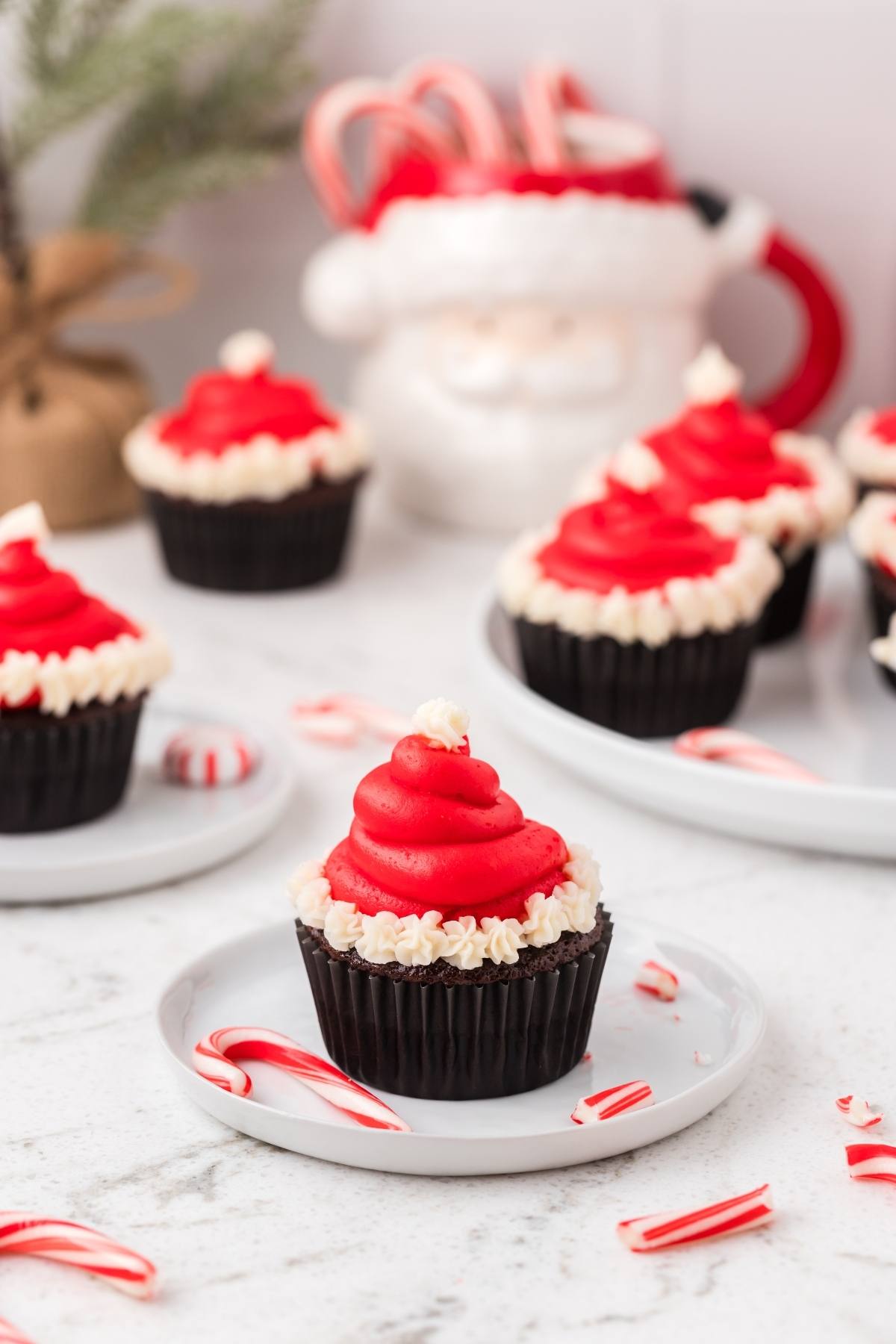 A chocolate cupcake with red frosting shaped like a Santa hat, surrounded by mini candy canes.