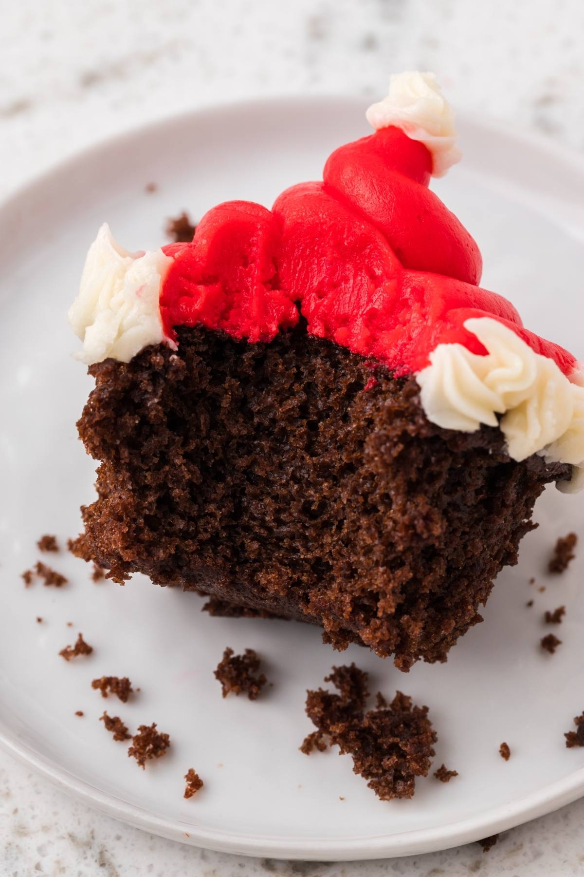 Partially eaten chocolate cupcake with red and white frosting on a white plate.