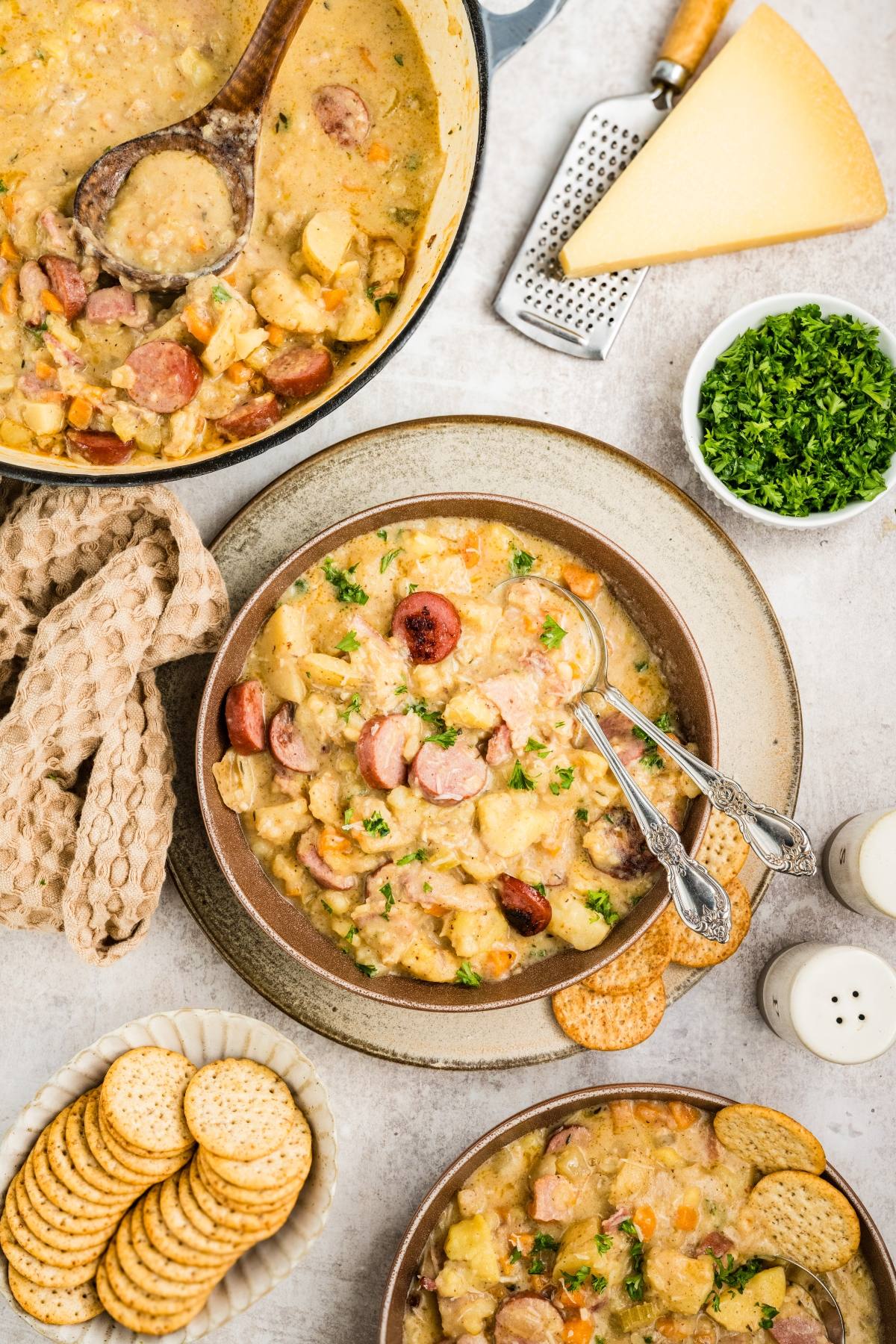 Two bowls of sausage and potato chowder, garnished with parsley, served with crackers and cheese on the side.