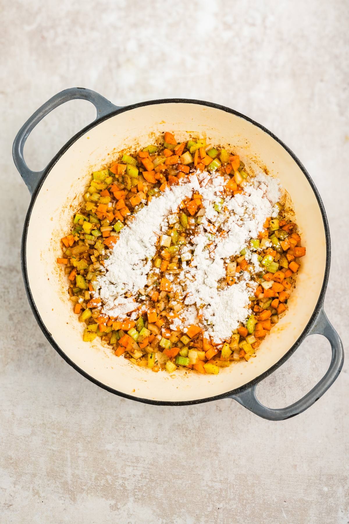 Chopped carrots, celery, and onions with flour in a large pot, ready to be mixed and cooked.