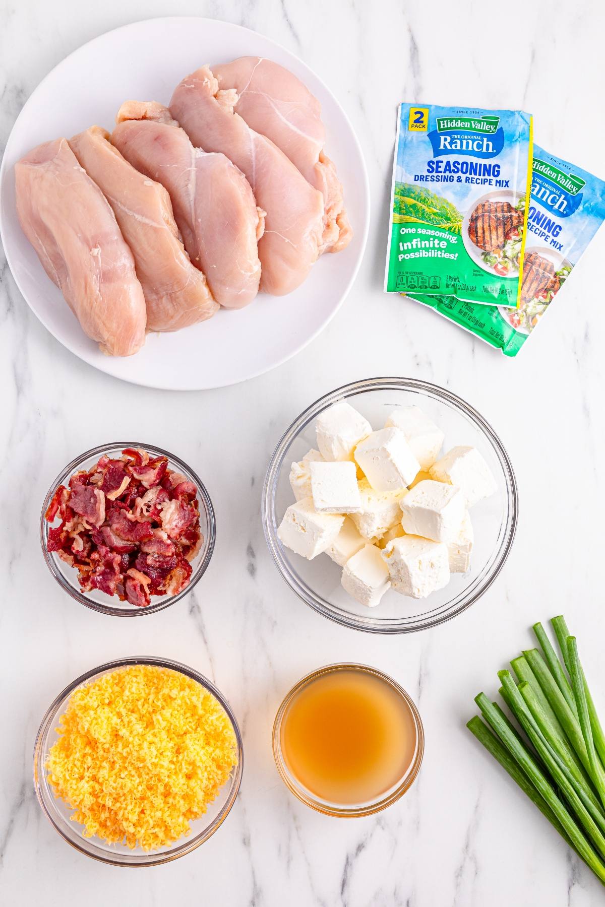 Raw chicken breasts, ranch seasoning packets, cooked bacon, cream cheese cubes, shredded cheese, broth, and green onions.