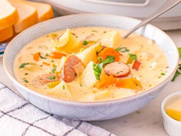 A bowl of creamy Slow Cooker Kielbasa Potato Soup with bread, parsley, and butter on the side.