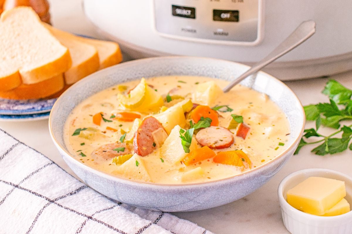 A bowl of creamy Slow Cooker Kielbasa Potato Soup served with bread slices, butter, and fresh herbs on the side.