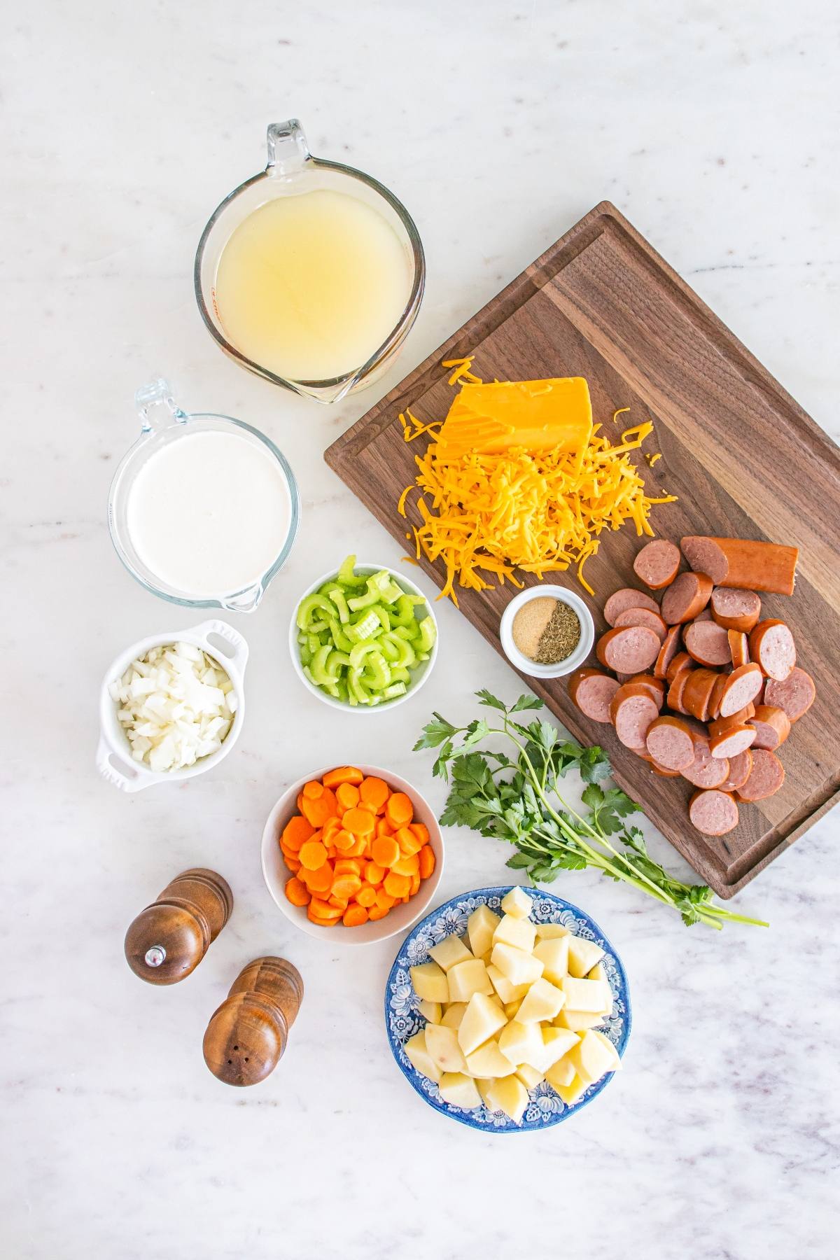 Ingredients for soup including broth, milk, cheddar cheese, sausage, potatoes, carrots, celery, onion, parsley, and pepper.