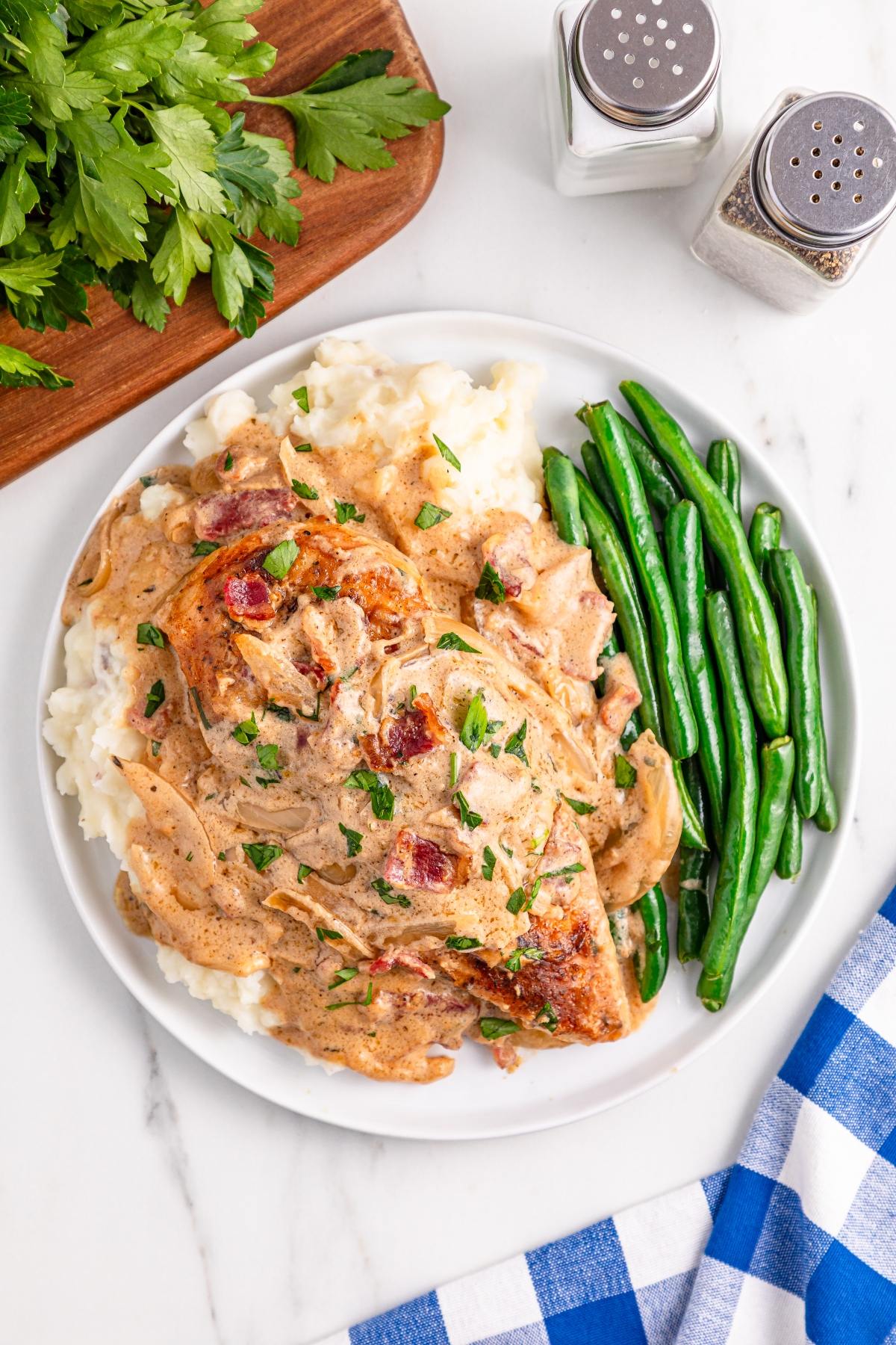 Chicken with creamy sauce on mashed potatoes, served with green beans on a white plate; salt and pepper nearby.