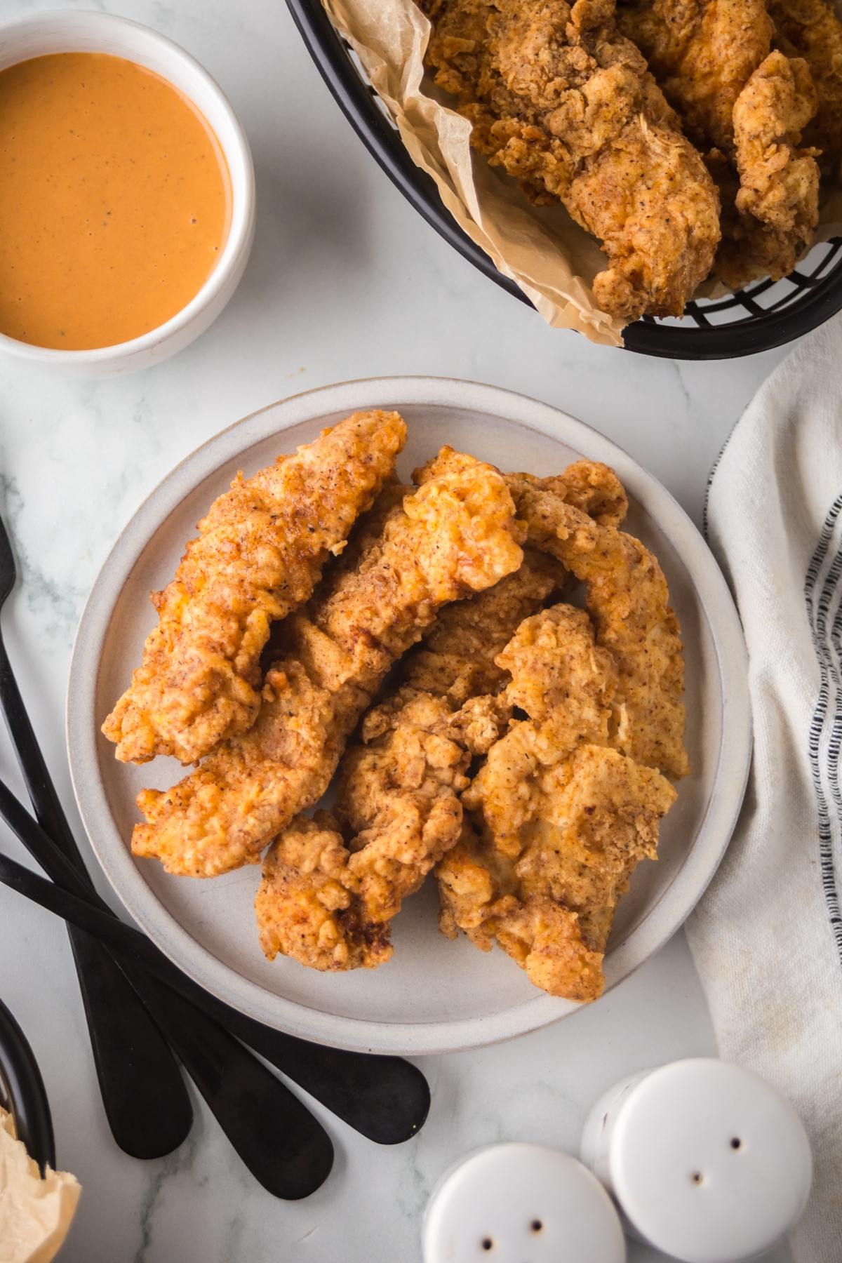 A plate of crispy fried chicken tenders with dipping sauce on the side.
