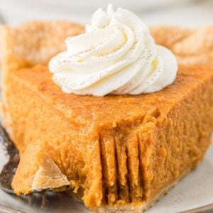 A slice of sweet potato pie topped with whipped cream sits on a plate, with a fork and a bite missing.