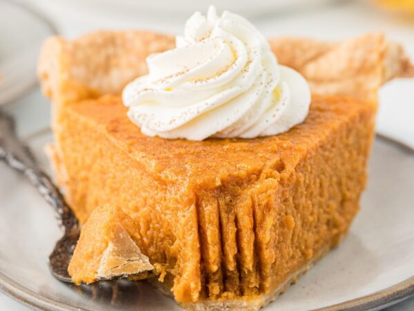 A slice of sweet potato pie topped with whipped cream sits on a plate, with a fork and a bite missing.