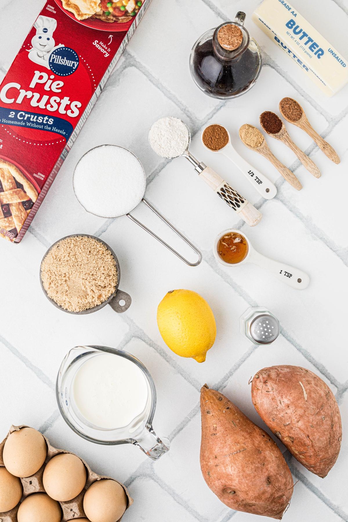 Sweet potato pie ingredients—pie crusts, eggs, sweet potatoes, lemon, milk, spices, sugar, flour, butter, and vanilla.