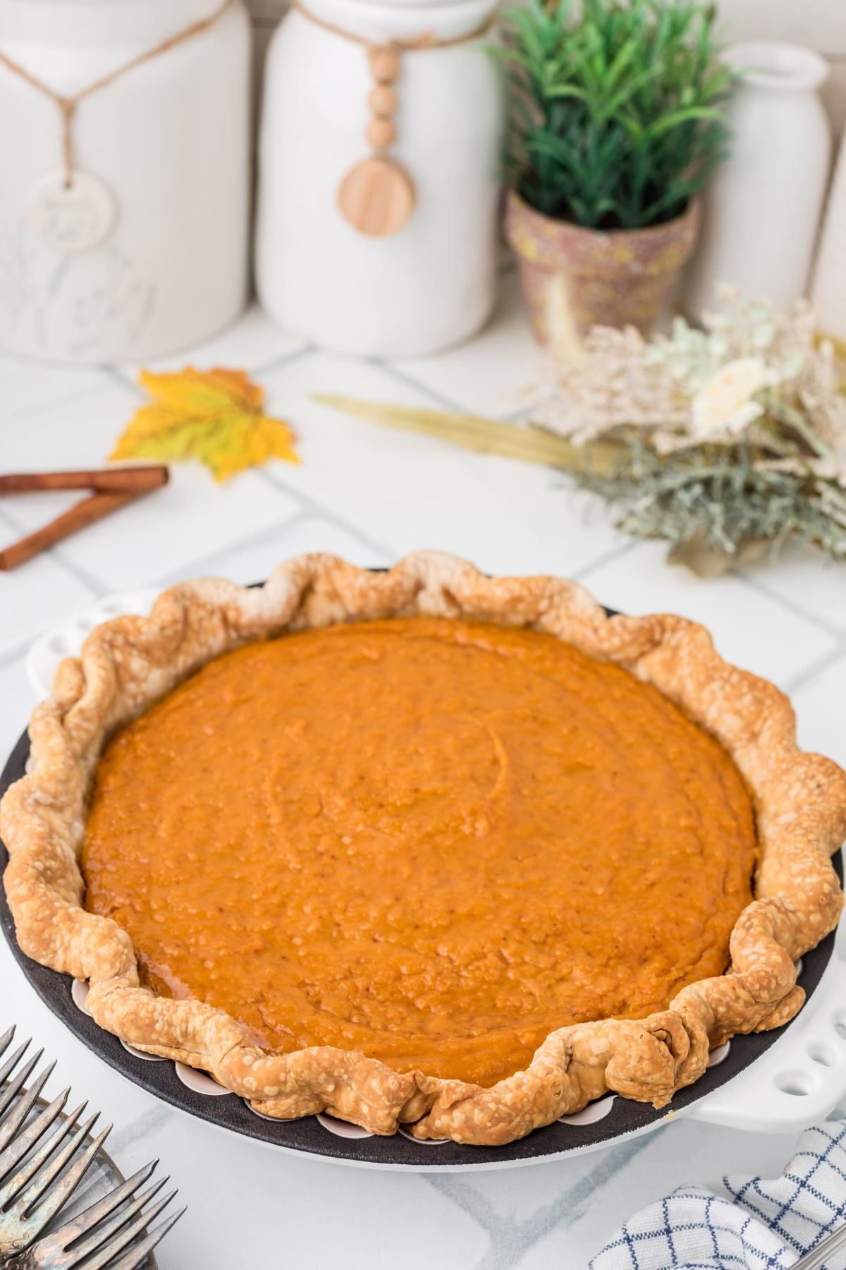 A homemade pumpkin pie with a golden crust sits on a white countertop, surrounded by fall decor.
