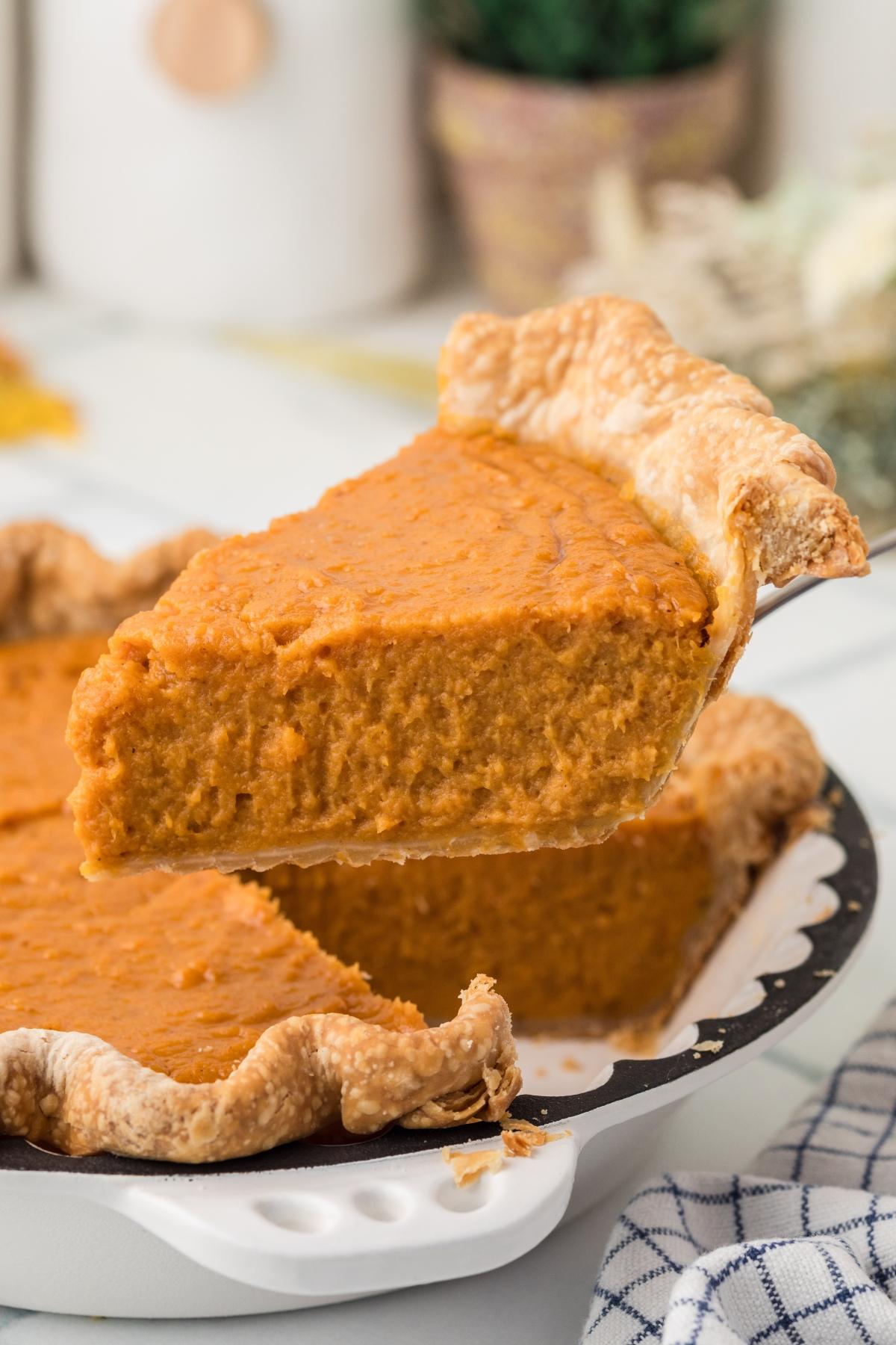 A slice of creamy orange sweet potato pie being lifted from a pie dish with a golden, flaky crust.